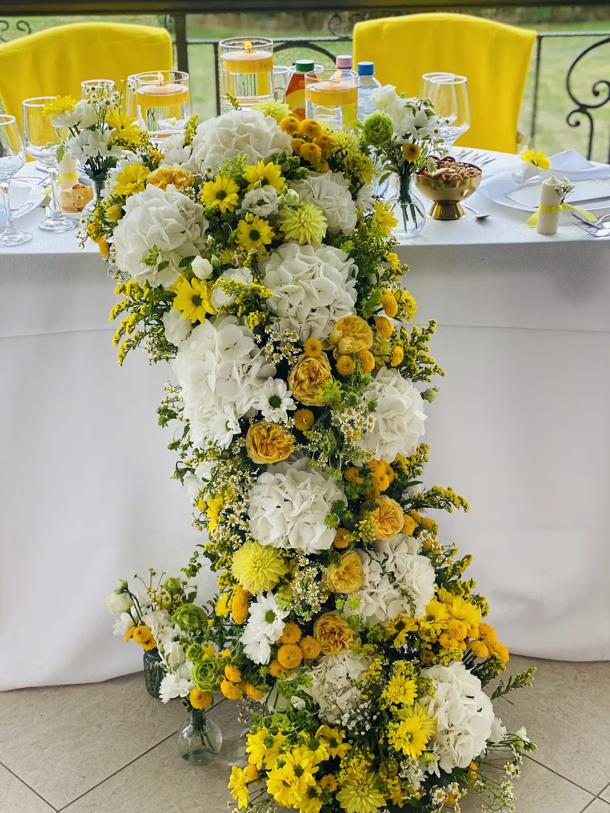 Coloană florală în galben și alb lângă masa mirilor