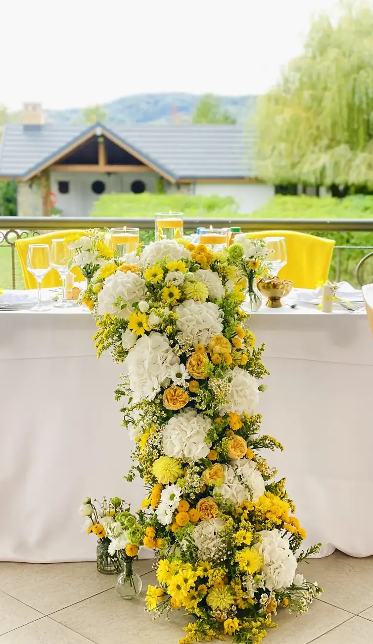 Coloană florală în galben și alb lângă masa mirilor