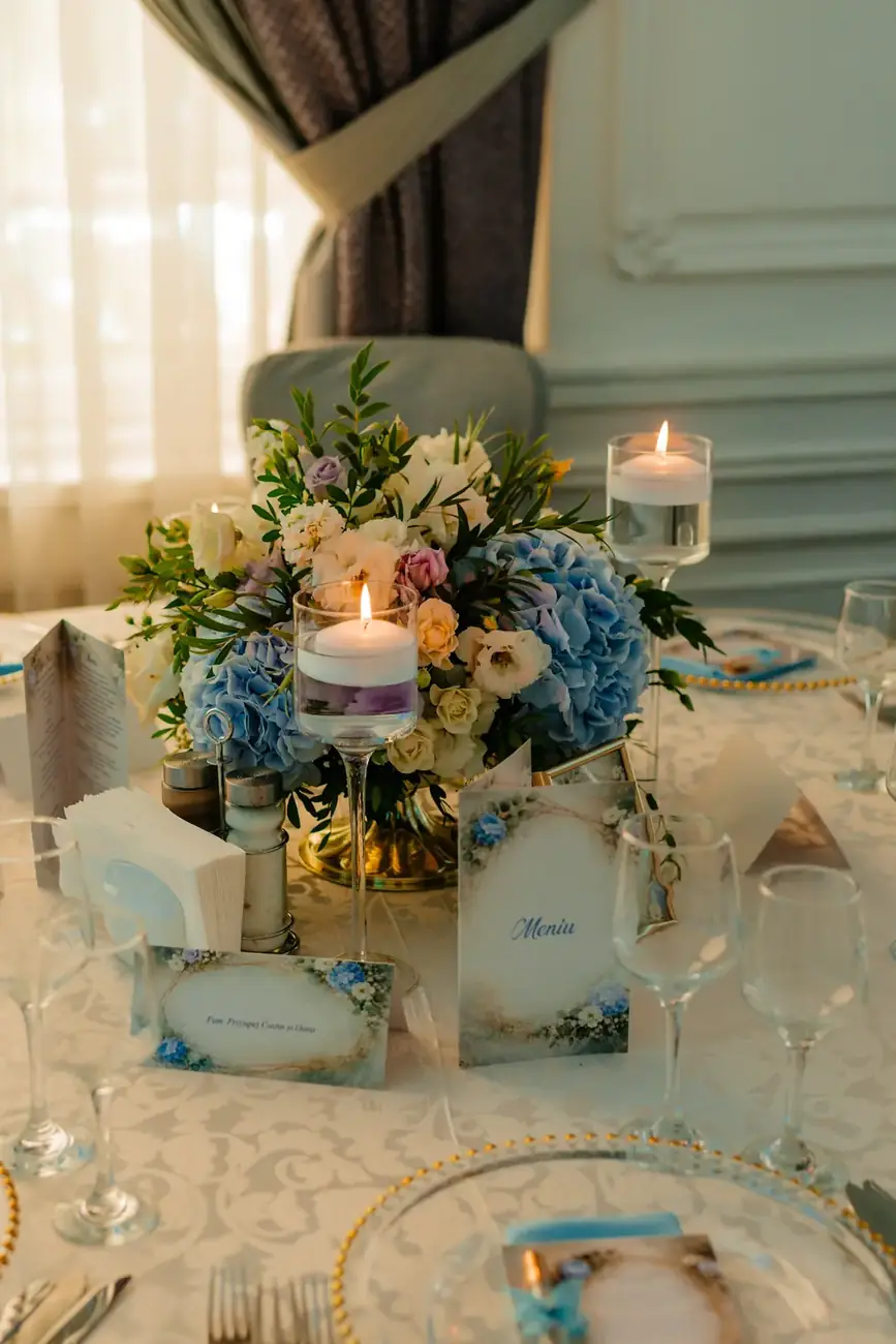 Lumânare și flori bleu pe masa invitaților