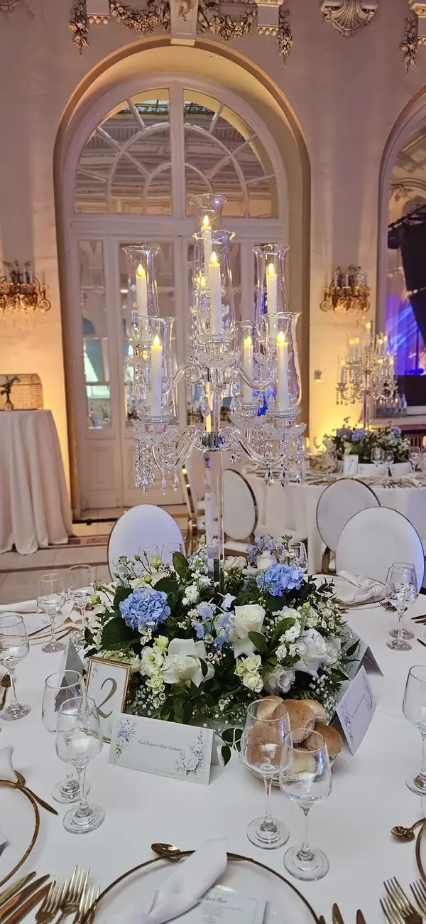 Masă cu flori bleu și ivoire, sub un candelabru cu lumânări